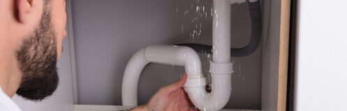 Plumber looking at a leaking sink pipe in an Apple Valley kitchen.