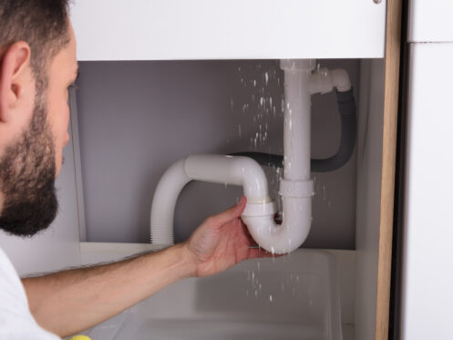 Plumber looking at a leaking sink pipe in an Apple Valley kitchen.